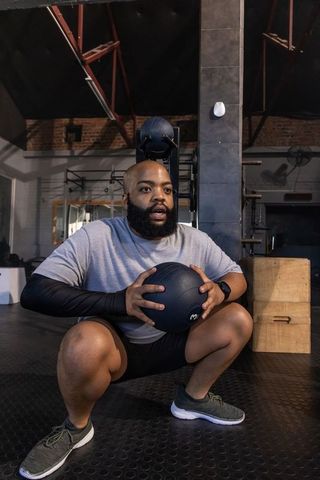 African man performing weighted squat holding medicine ball in industrial gym training