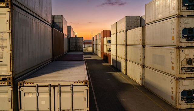 Sunset shipping container corridor with stacked reefers, freight yard alley, long shadows