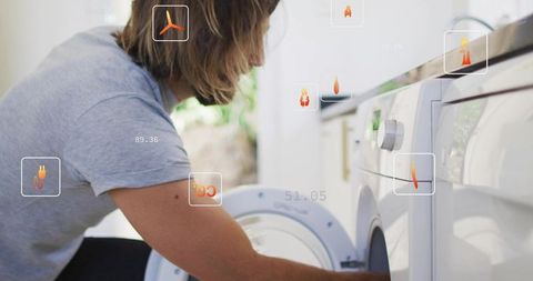 Kneeling man checking front-load washer with augmented reality overlays in modern laundry