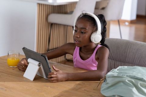 African american girl learning with tablet and headphones at home kitchen table morning routine