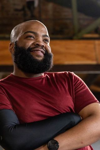 Smiling african american bald man crossing arms in studio wearing maroon t-shirt and watch