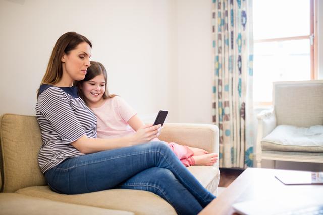 Mother and daughter using mobile in living room at home