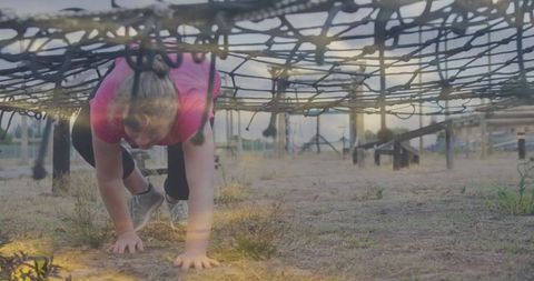 Determined Athlete Crawling Under Cargo Net in Fitness Challenge