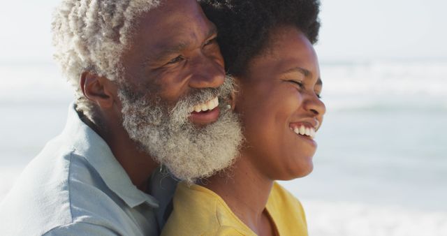 Elderly man with white beard and young woman embracing on a sunlit beach, smiling and bonding. Ideal for family lifestyle, senior living, intergenerational relationships, summer vacations, or happy moments themes. Can be used in advertisements, websites showcasing family values, healthcare, and travel.