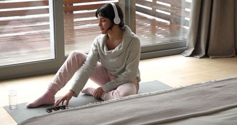 Relaxed Woman in Lounge Wear Streaming Music on Yoga Mat by Glass Doors