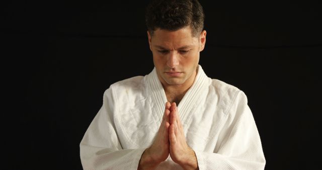 Martial artist wearing white uniform practicing a traditional bowing gesture with hands together, showcasing discipline and focus. Used for themes of mindfulness, respect, martial arts practice, or cultural traditions.