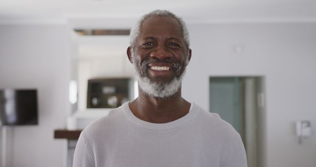 Cheerful senior man with gray hair happily smiling in bright room. Suitable for advertisements relating to healthy aging, happiness, active lifestyles for seniors, and family-oriented content.