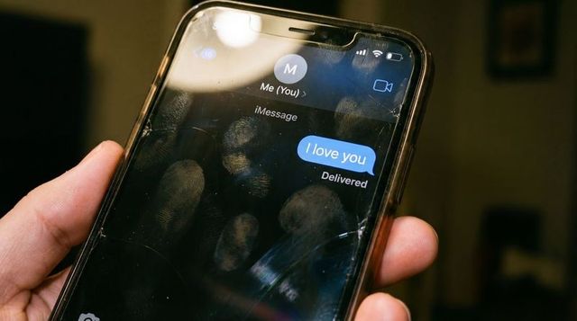 Hand holding cracked smartphone showing 'I love you' blue message bubble on smudged screen