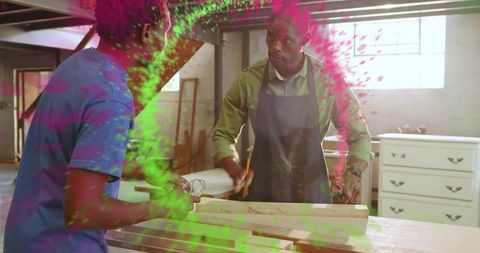 Two woodworkers marking wooden planks at workshop bench wearing aprons and safety glasses