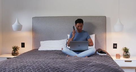 Man Balances Smartphone and Laptop on Comfortable Modern Bed