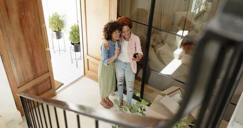 African american women embracing while checking smartphone in new home entryway
