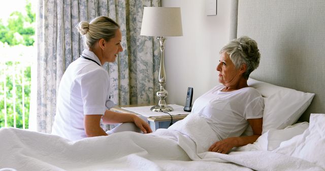 Nurse sitting beside senior woman offering care and comfort. Home care services for elderly patients. Ideal for use in healthcare, nursing, elderly care, medical services, and home caregiving promotional materials.