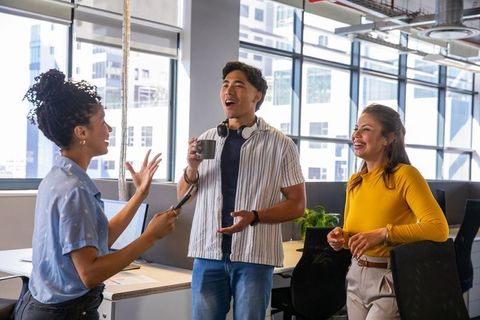 Young multicultural team laughing and chatting in modern open-plan office with coffee