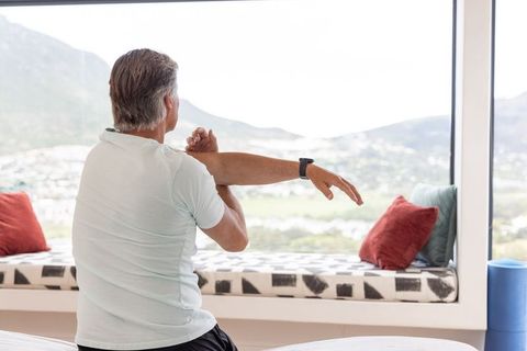 African american senior man stretching on window seat with smartwatch and panoramic view