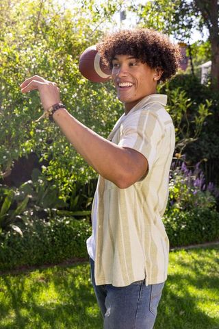 Young man throwing football in sunny backyard garden enjoying active summer lifestyle