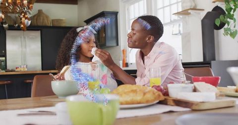 Father wiping daughter's mouth during cozy family breakfast sharing toast and pastries