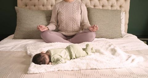 Mother meditating while baby sleeps peacefully on bed