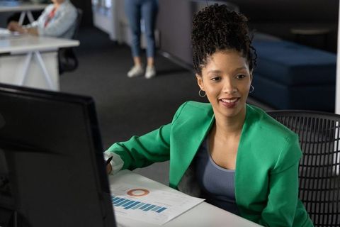 African american woman in green blazer reviewing charts and data at office workstation