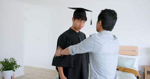 Proud Father Helping Son Prepare for Graduation Ceremony