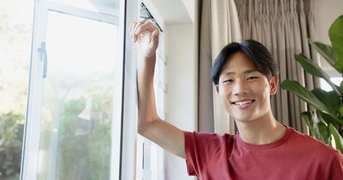 Asian Teen Smiling by Window with Natural Light and Home Ambiance