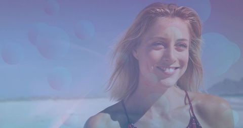 Smiling woman enjoying sunny beach day with windblown hair, strappy swim top and bokeh