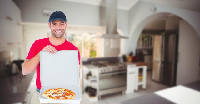 Smiling delivery man in red uniform holding an open pizza box in a modern kitchen. Ideal for use in advertisements for food delivery services, restaurant promotions, or articles about convenience and fast food. The modern kitchen setting emphasizes a home delivery context.
