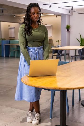 African american woman standing at coworking table working on laptop in modern office