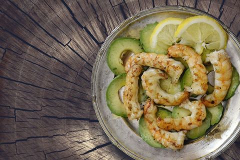 Grilled prawns with avocado and lemon garnish on rustic wood