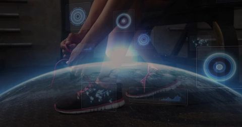 Midadult woman tying pink-laced running shoes in gym with holographic globe hud overlay