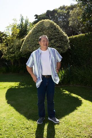 Mature asian man standing and smiling in sunny backyard wearing striped shirt casual lifestyle