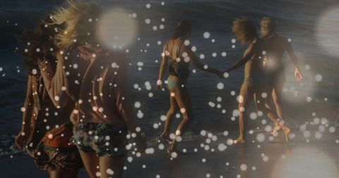 Sunlit friends walking into surf at golden hour beach with bokeh light effects