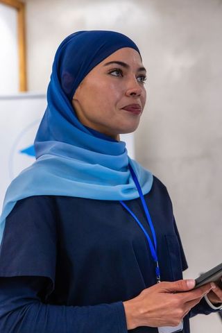 Confident professional woman in blue headscarf presenting with tablet at conference