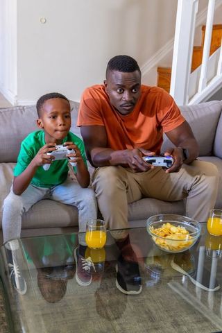 African American father and son playing video games on couch, competition and family bonding