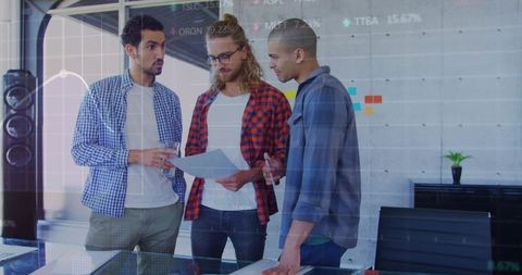 Startup team collaborating over analytics printouts in modern office with data overlay
