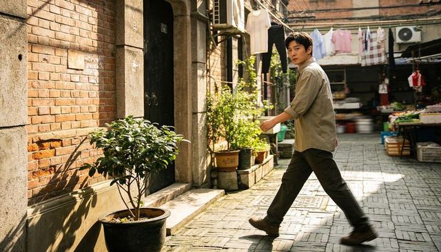 Man walking through sunlit urban alley with potted plants and market stalls
