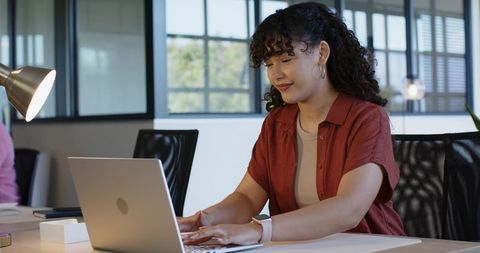 African american woman typing on laptop at modern office desk, productivity and focus