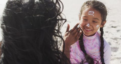 Mother applying sunscreen to daughter's face on sunny beach