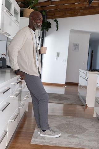 Mature african man leaning on white countertop holding mug, modern kitchen lifestyle