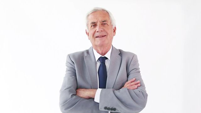 Elderly Caucasian man in a business suit standing with arms crossed against white background. Ideal for depicting confidence, experience, and executive leadership in corporate settings. Suitable for business presentations, company profiles, corporate advertising, and leadership articles.