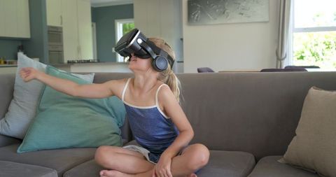 Young girl wearing vr headset reaching forward while sitting on sofa
