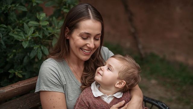 Smiling mother holding toddler on park bench, warm bonding family portrait outdoors