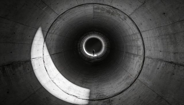 Solitary silhouette standing at distant light inside concrete cylinder with crescent light