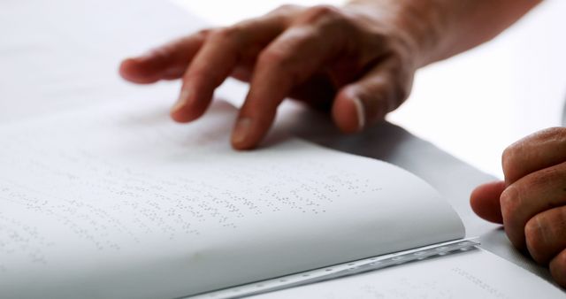 Hands reading Braille on white paper. Can be used for illustrating accessibility, education for the visually impaired, and inclusive communication. Ideal for articles, educational materials, and campaigns supporting disability awareness.