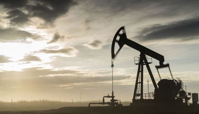 Sunset pumpjack silhouette extracting crude on rural oil pad