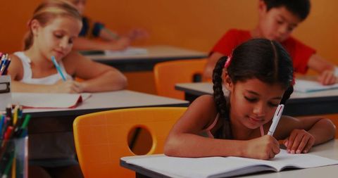 Elementary girl writing at classroom desk braided hair focused learning with colorful pencils