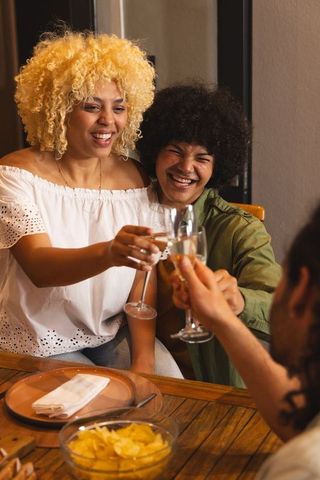 Friends clinking champagne glasses laughing at cozy casual dinner party celebration together