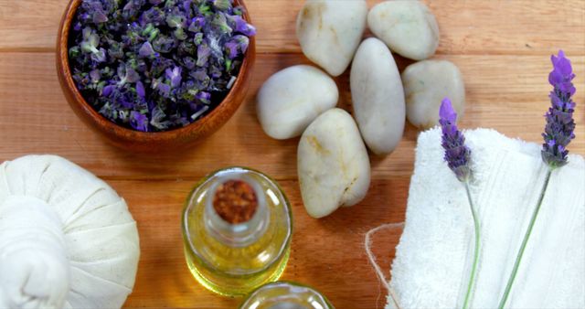 A variety of spa items including lavender flowers, massage oils, and smooth stones are arranged on a wooden surface, with copy space. These elements are commonly used in aromatherapy and relaxation treatments to promote well-being and stress relief.