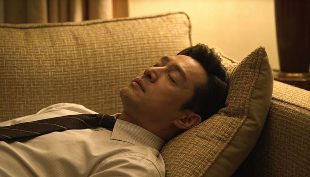 Businessman resting on sofa after long workday, relaxing in warm ambient living room light