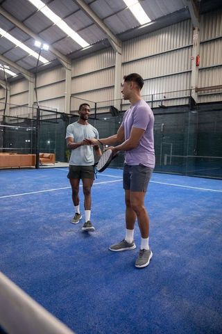 Shaking hands after padel match on indoor blue court, mixed-race friends training together