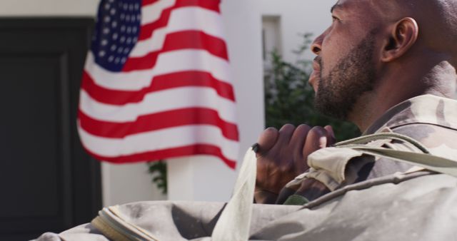 African American soldier in camouflage uniform relaxing and reflecting with American flag in background. This visual symbolizes patriotism, dedication, and bravery, representing military service and sacrifice. Ideal for use in campaigns, advertisements, and articles related to Veterans Day, military recruitment, patriotic events, and support for troops.